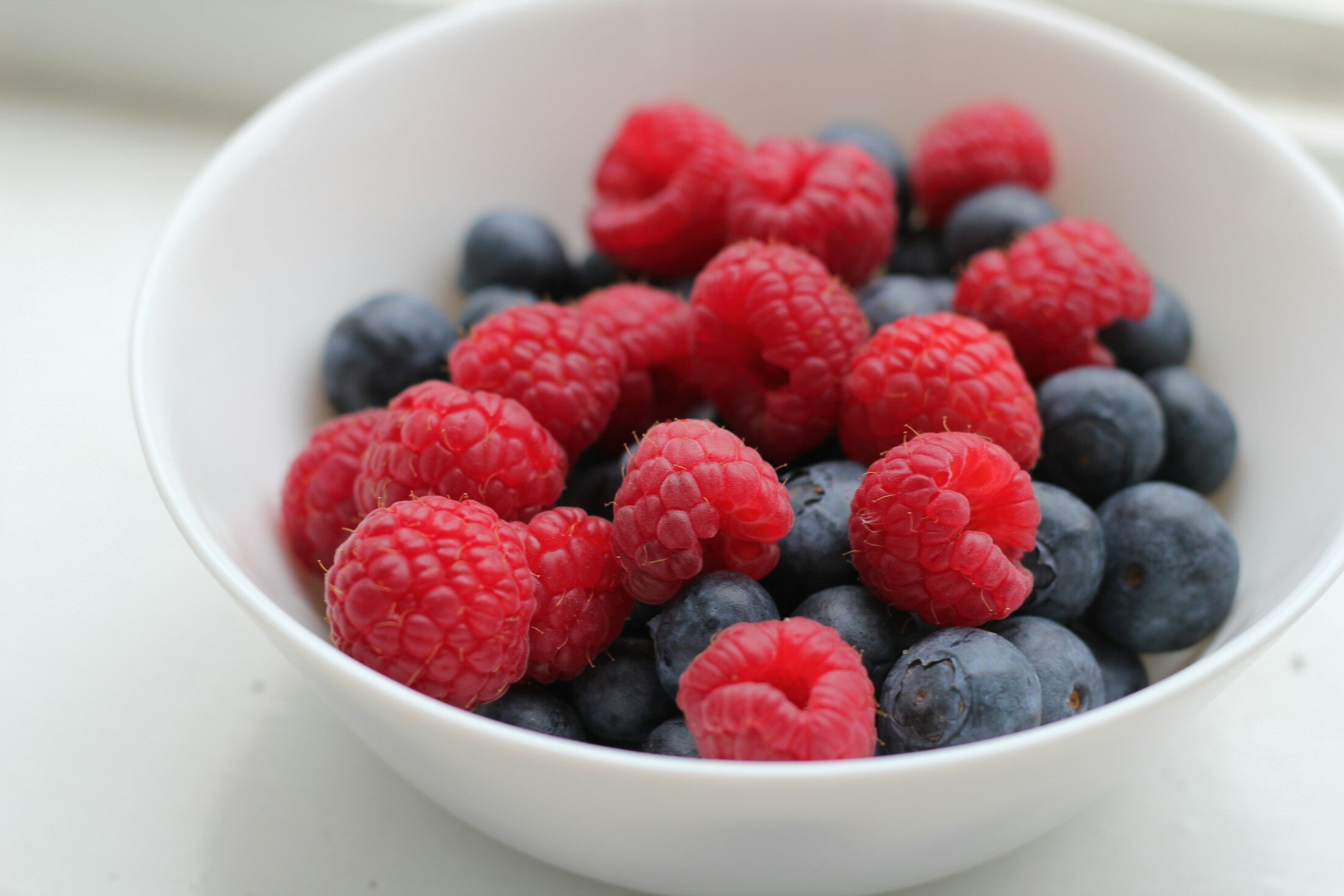 Photo by Almira Yausheva a white bowl filled with raspberries and blueberries